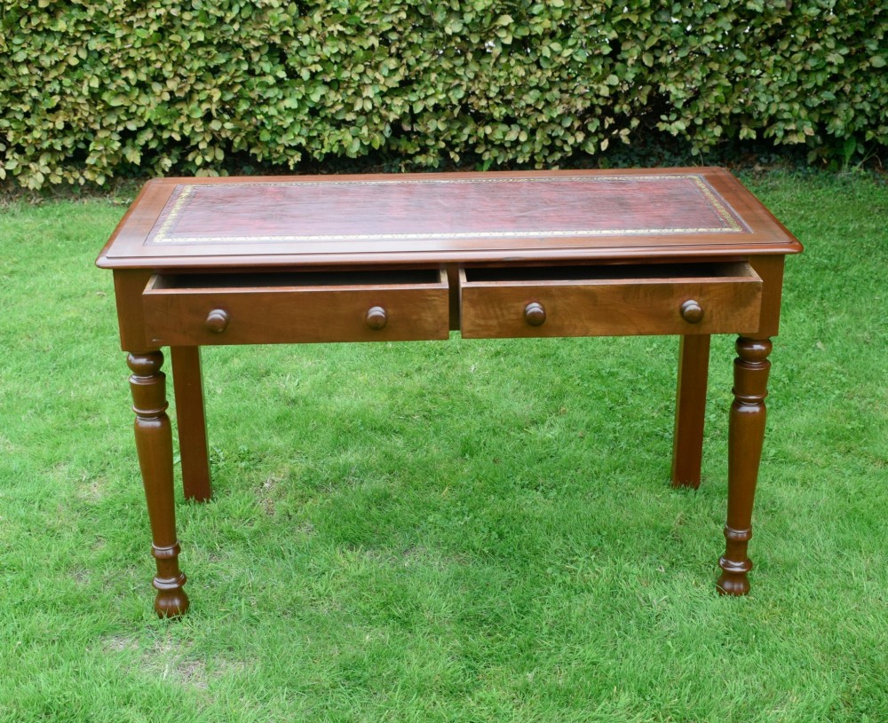 A Victorian mahogany writing table with a red leather inset surface, two drawers with wooden knob handles, turned front legs, and square back legs. View VII