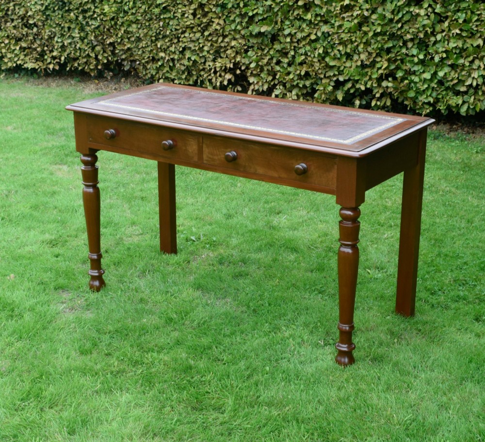 A Victorian mahogany writing table with a red leather inset surface, two drawers with wooden knob handles, turned front legs, and square back legs. View VIII