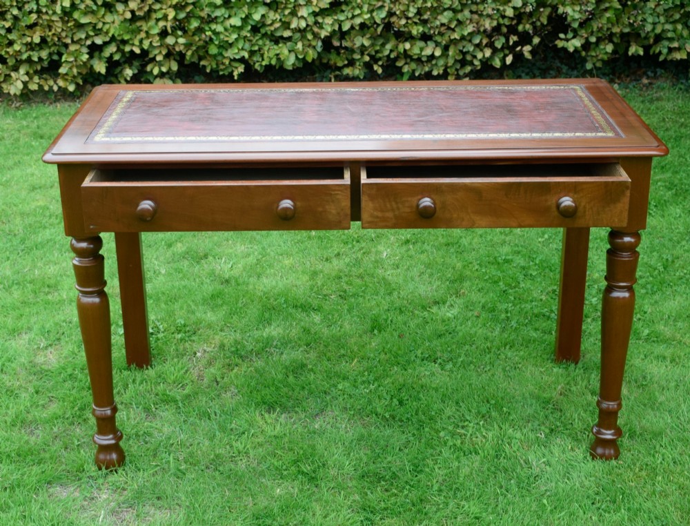 A Victorian mahogany writing table with a red leather inset surface, two drawers with wooden knob handles, turned front legs, and square back legs. View IX