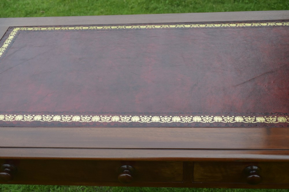 A Victorian mahogany writing table with a red leather inset surface, two drawers with wooden knob handles, turned front legs, and square back legs. View X