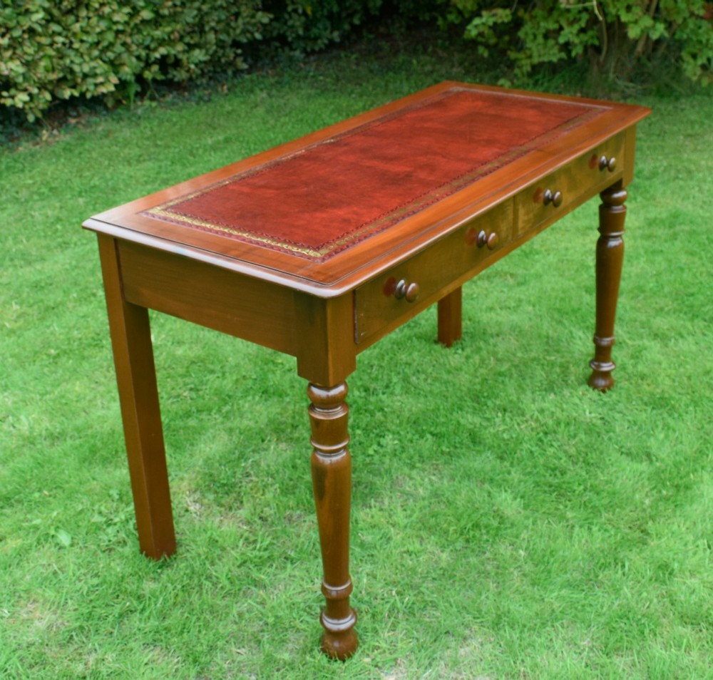 A Victorian mahogany writing table with a red leather inset surface, two drawers with wooden knob handles, turned front legs, and square back legs. View XIII