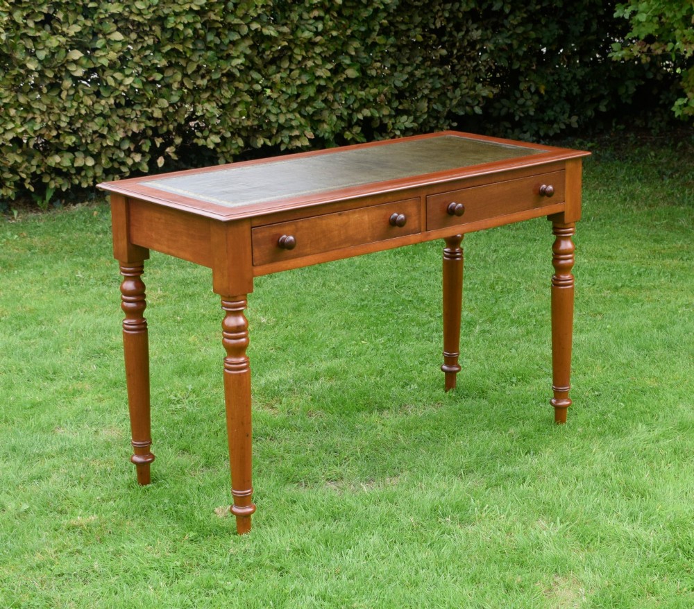 A Victorian warm brown mahogany writing table featuring an inset green leather writing surface, two drawers with knob handles, and turned legs.