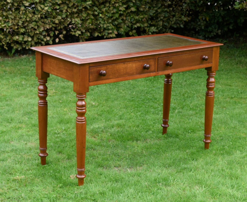 A Victorian warm brown mahogany writing table featuring an inset green leather writing surface, two drawers with knob handles, and turned legs. View II