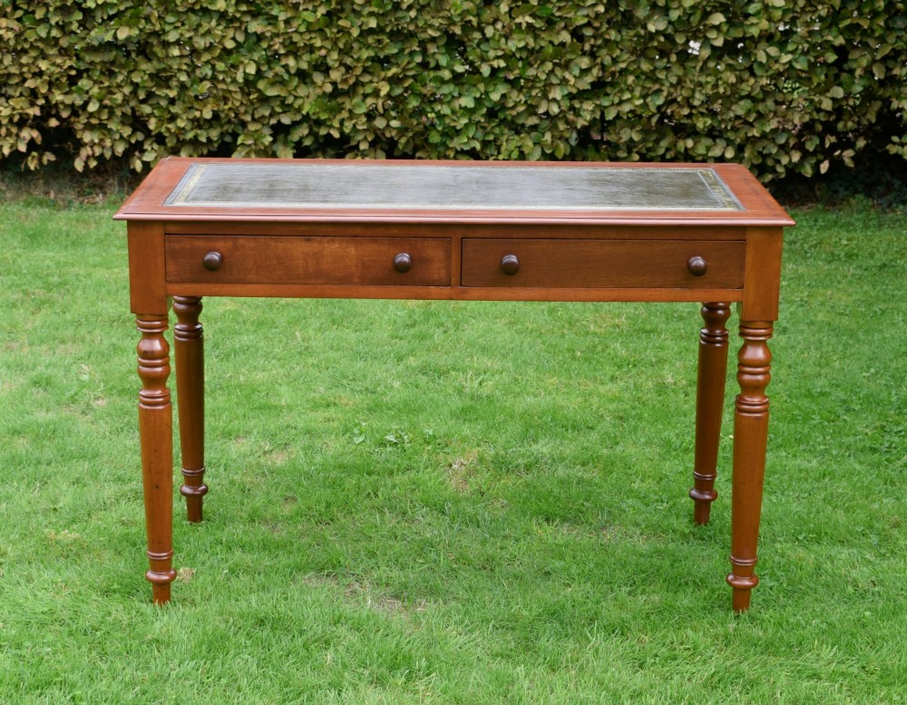 A Victorian warm brown mahogany writing table featuring an inset green leather writing surface, two drawers with knob handles, and turned legs. View III