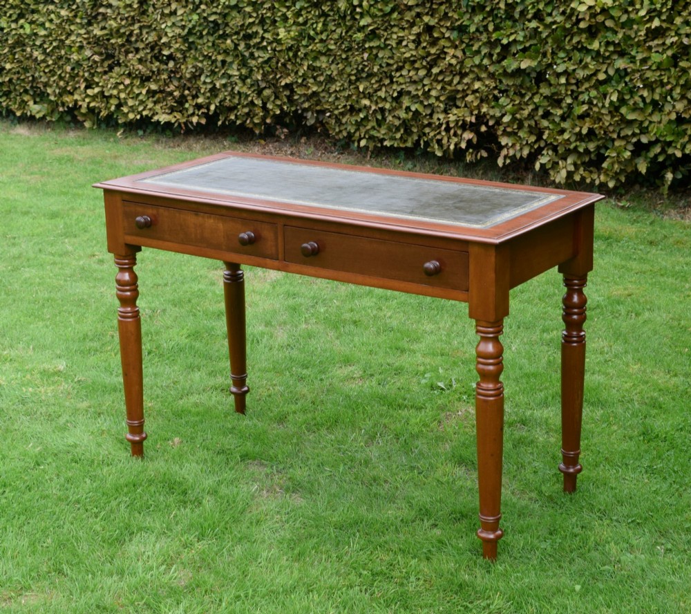 A Victorian warm brown mahogany writing table featuring an inset green leather writing surface, two drawers with knob handles, and turned legs. View IV
