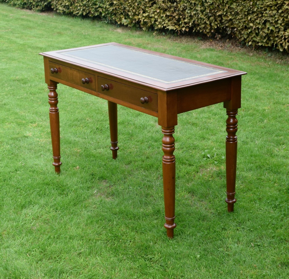 A Victorian warm brown mahogany writing table featuring an inset green leather writing surface, two drawers with knob handles, and turned legs. View V