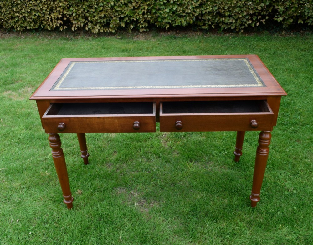 A Victorian warm brown mahogany writing table featuring an inset green leather writing surface, two drawers with knob handles, and turned legs. View VIII