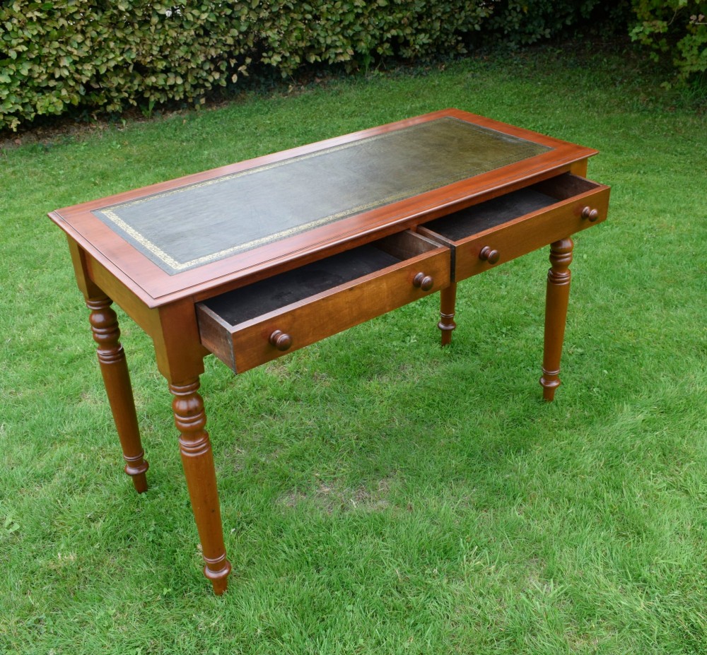 A Victorian warm brown mahogany writing table featuring an inset green leather writing surface, two drawers with knob handles, and turned legs. View IX