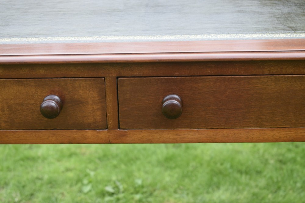 A Victorian warm brown mahogany writing table featuring an inset green leather writing surface, two drawers with knob handles, and turned legs. View XI