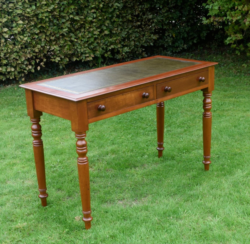 A Victorian warm brown mahogany writing table featuring an inset green leather writing surface, two drawers with knob handles, and turned legs. View XIV
