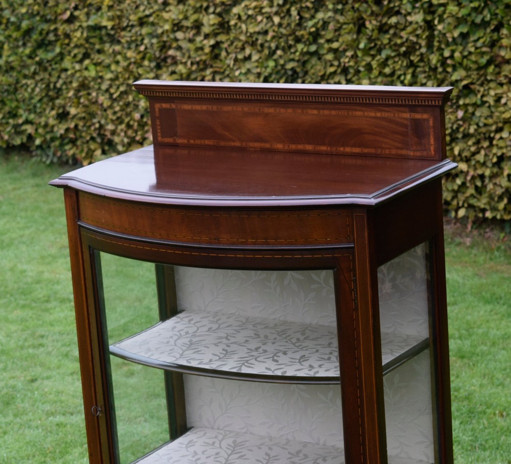 An Edwardian mahogany bowfront display cabinet featuring curved glass doors, satinwood string inlay, lined interior shelves, and tapered square legs. View V