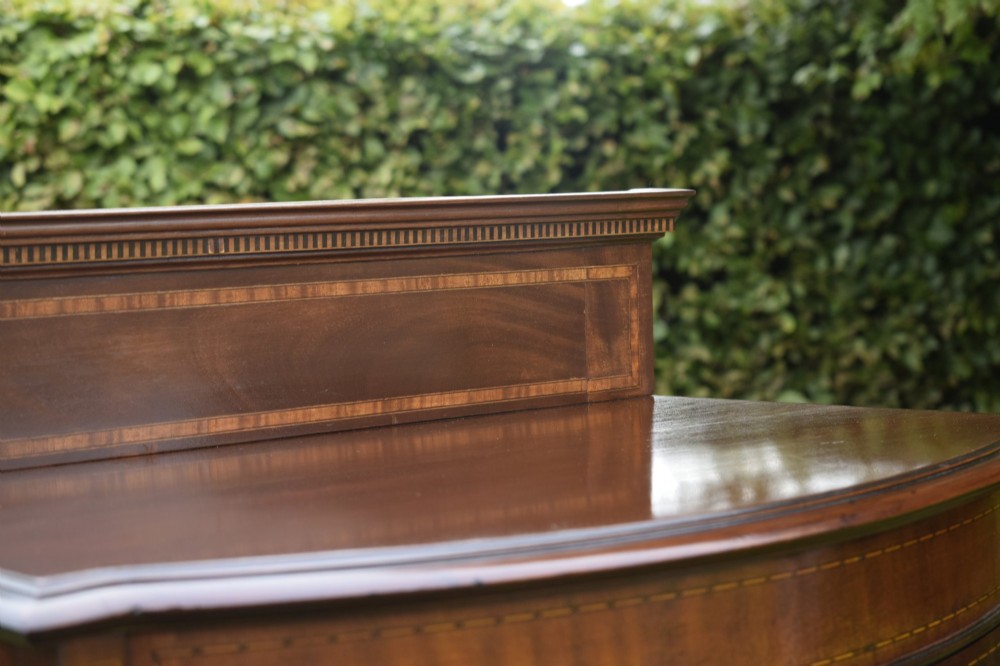 An Edwardian mahogany bowfront display cabinet featuring curved glass doors, satinwood string inlay, lined interior shelves, and tapered square legs. View IX