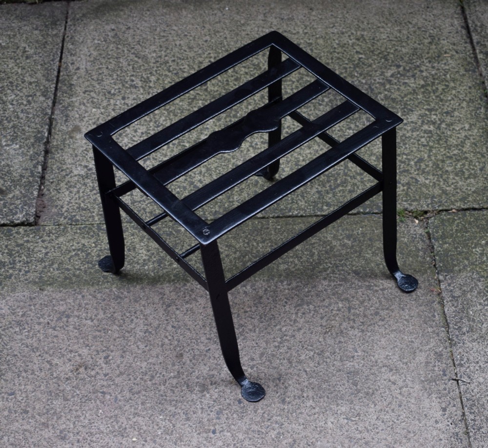 A black wrought iron fireplace footman featuring a slatted top with a central decorative cutout handle, resting on four curved legs with flat circular feet. View II
