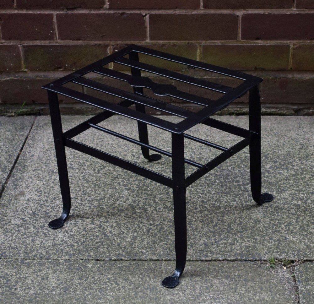 A black wrought iron fireplace footman featuring a slatted top with a central decorative cutout handle, resting on four curved legs with flat circular feet. View IV