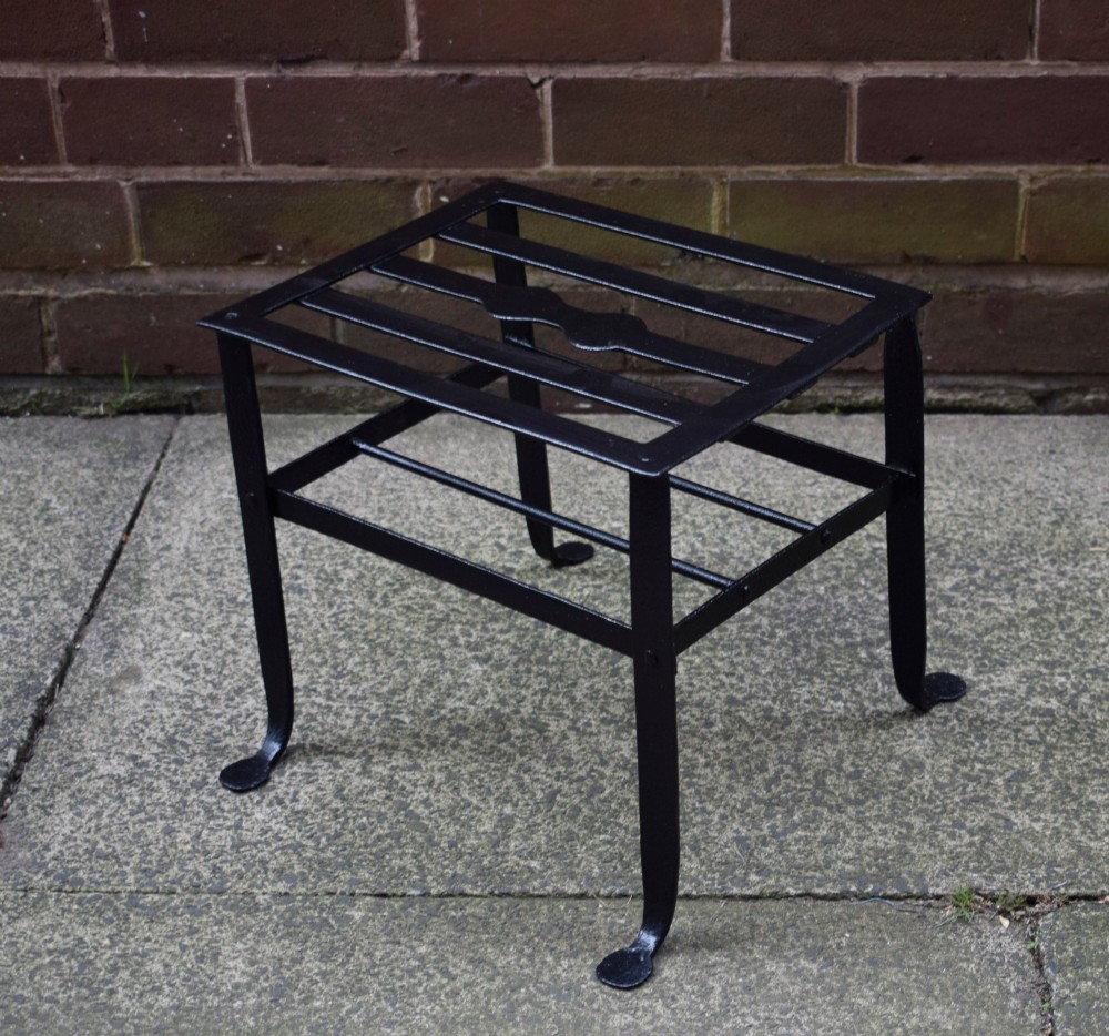 A black wrought iron fireplace footman featuring a slatted top with a central decorative cutout handle, resting on four curved legs with flat circular feet. View IX