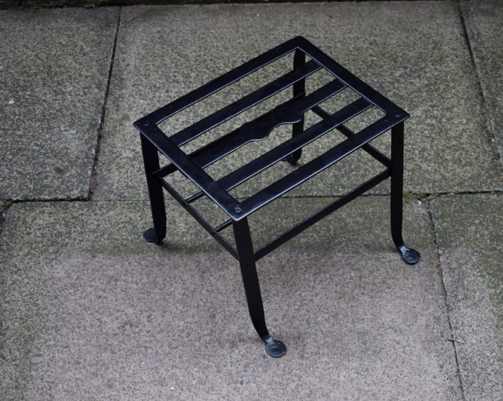 A black wrought iron fireplace footman featuring a slatted top with a central decorative cutout handle, resting on four curved legs with flat circular feet. View XI