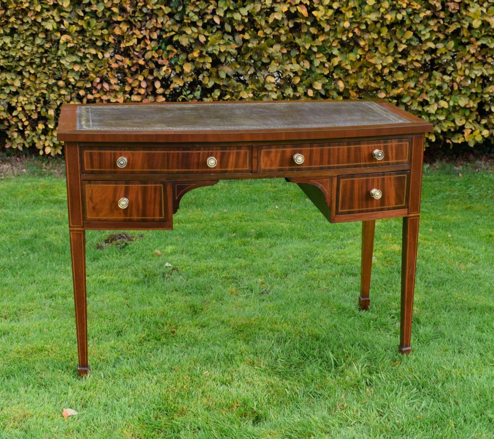 An Edwardian inlaid mahogany writing desk featuring a green leather inset top with gold tooling, four drawers with brass handles, and square tapered legs. View III