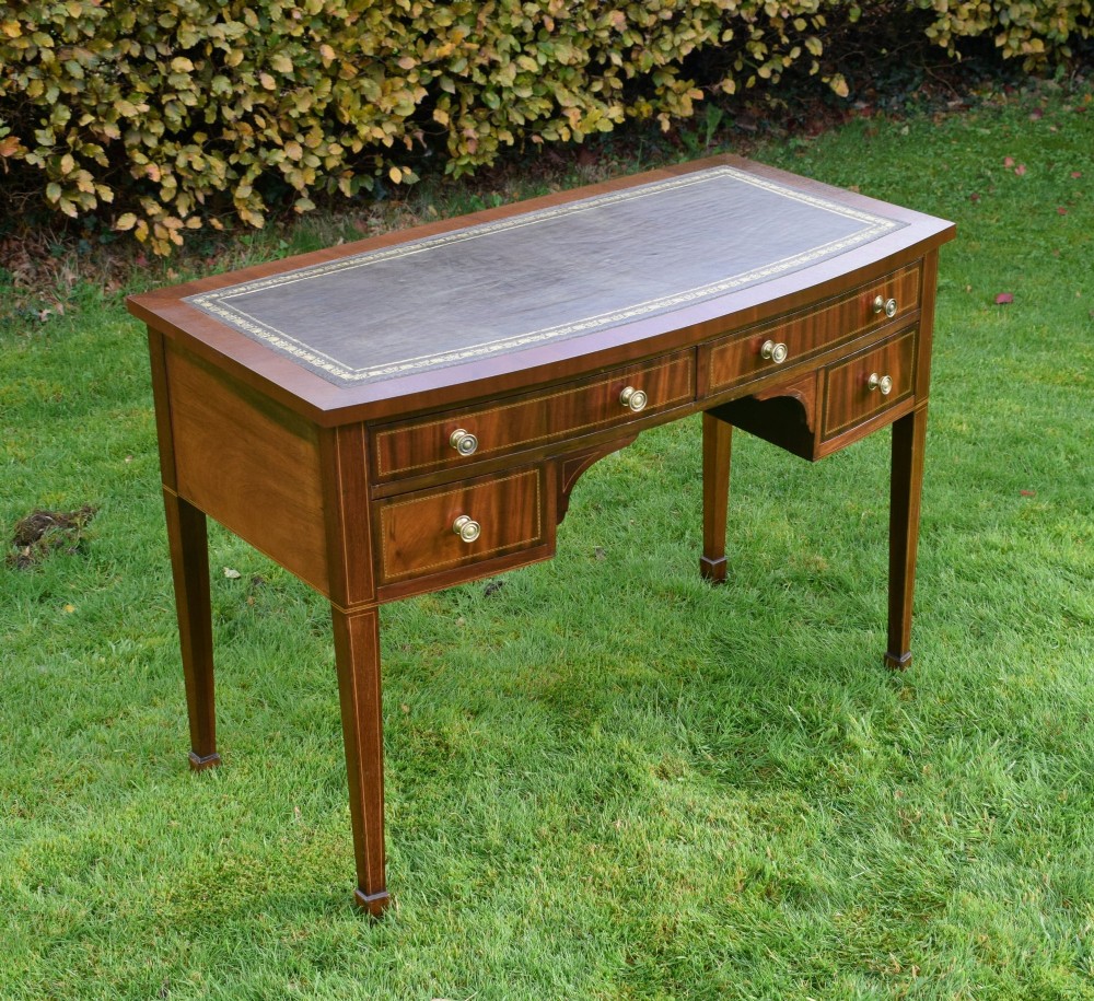 An Edwardian inlaid mahogany writing desk featuring a green leather inset top with gold tooling, four drawers with brass handles, and square tapered legs. View IV