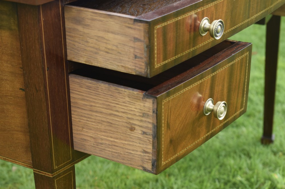 An Edwardian inlaid mahogany writing desk featuring a green leather inset top with gold tooling, four drawers with brass handles, and square tapered legs. View V