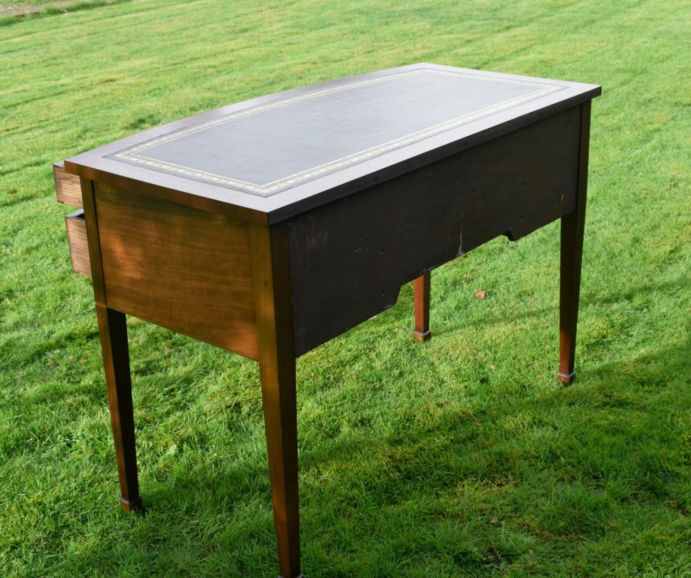 An Edwardian inlaid mahogany writing desk featuring a green leather inset top with gold tooling, four drawers with brass handles, and square tapered legs. View VI