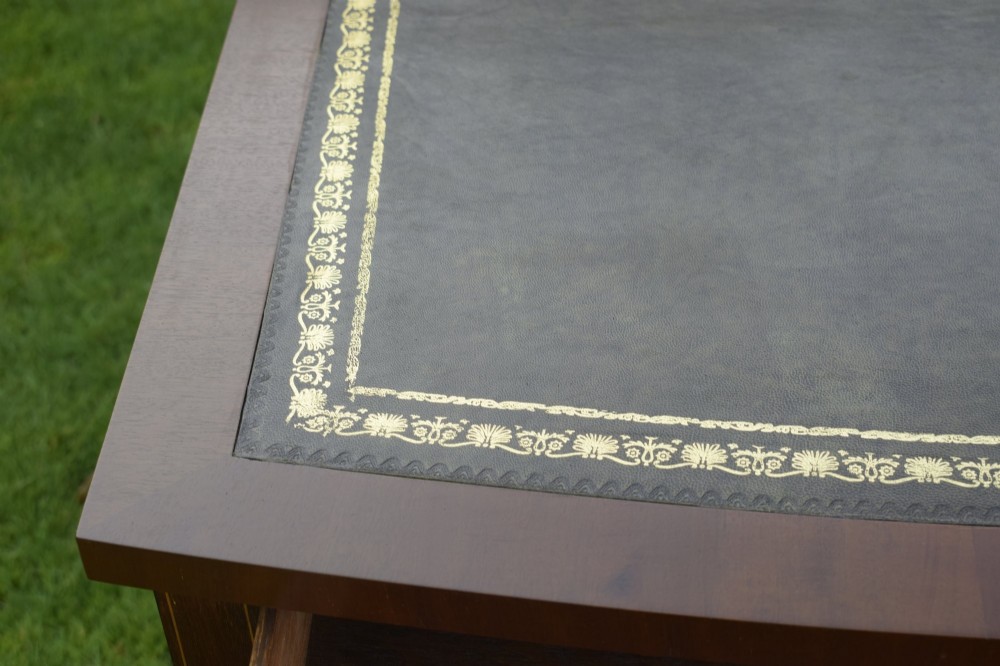 An Edwardian inlaid mahogany writing desk featuring a green leather inset top with gold tooling, four drawers with brass handles, and square tapered legs. View VII