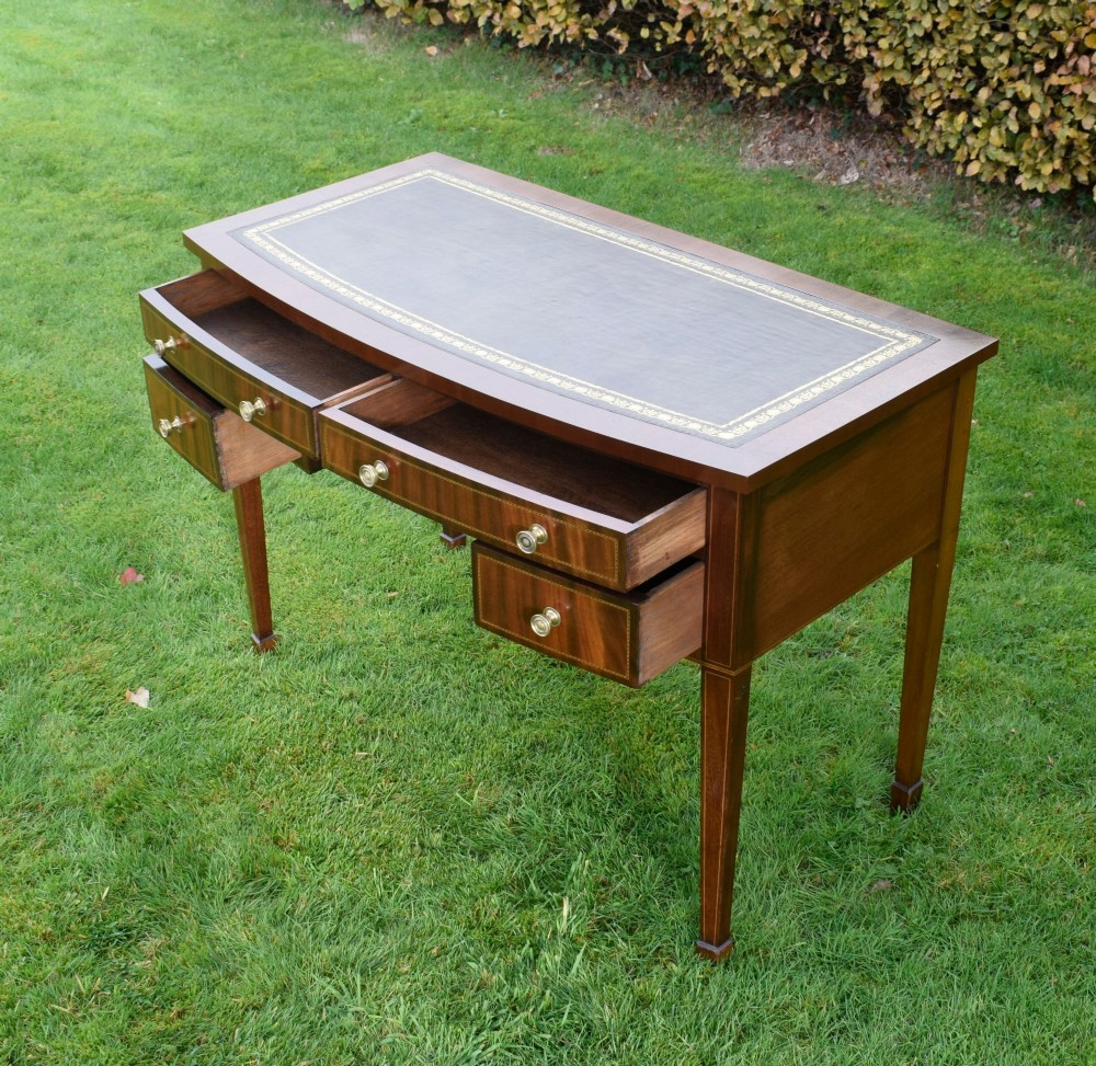 An Edwardian inlaid mahogany writing desk featuring a green leather inset top with gold tooling, four drawers with brass handles, and square tapered legs. View IX