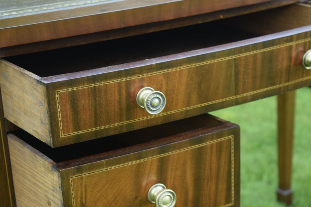 An Edwardian inlaid mahogany writing desk featuring a green leather inset top with gold tooling, four drawers with brass handles, and square tapered legs. View X
