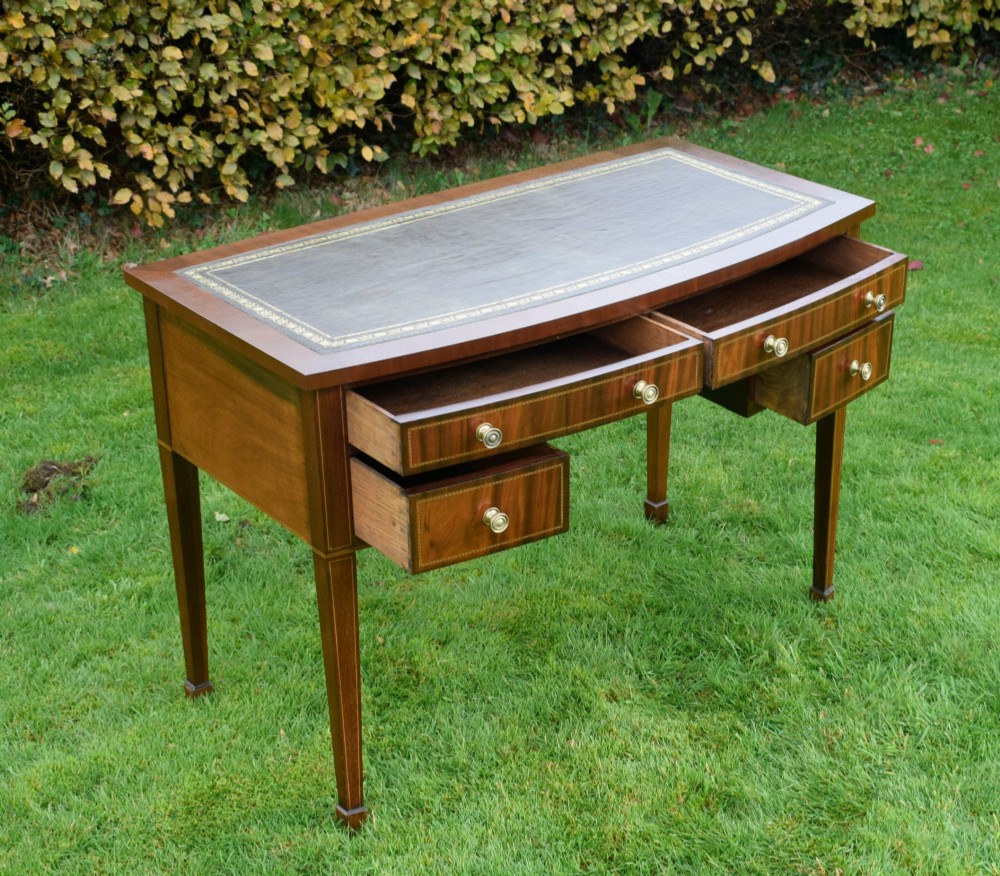 An Edwardian inlaid mahogany writing desk featuring a green leather inset top with gold tooling, four drawers with brass handles, and square tapered legs. View XI