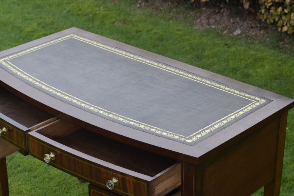 An Edwardian inlaid mahogany writing desk featuring a green leather inset top with gold tooling, four drawers with brass handles, and square tapered legs. View XII