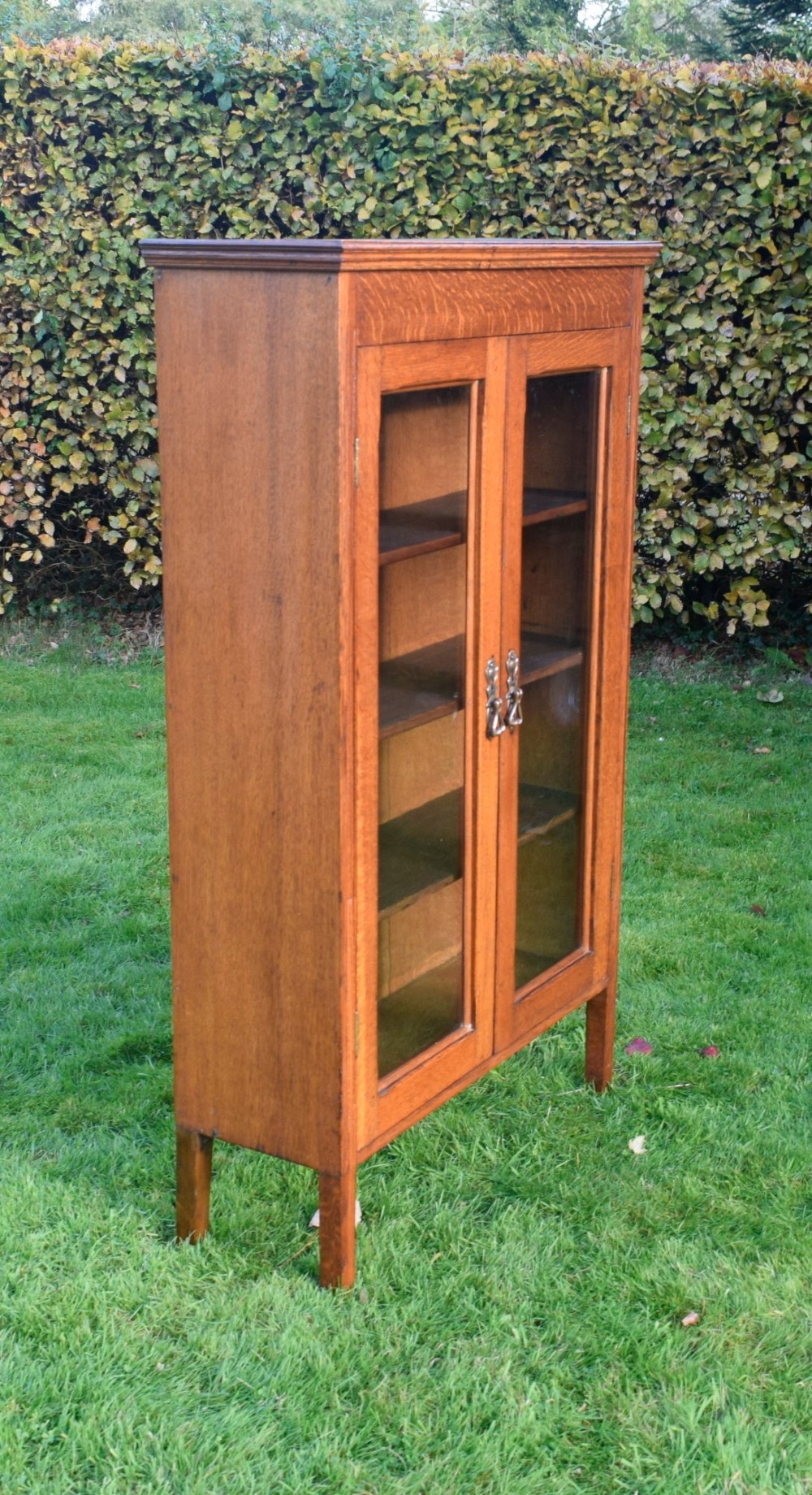 An early twentieth-century warm brown oak bookcase featuring twin glazed doors, brass hardware, and three internal shelves. View III