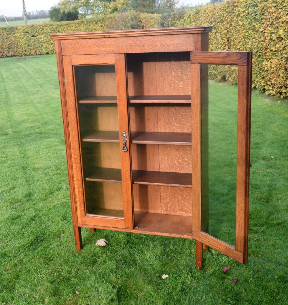 An early twentieth-century warm brown oak bookcase featuring twin glazed doors, brass hardware, and three internal shelves. View V