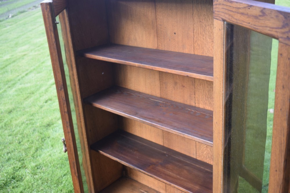 An early twentieth-century warm brown oak bookcase featuring twin glazed doors, brass hardware, and three internal shelves. View VII
