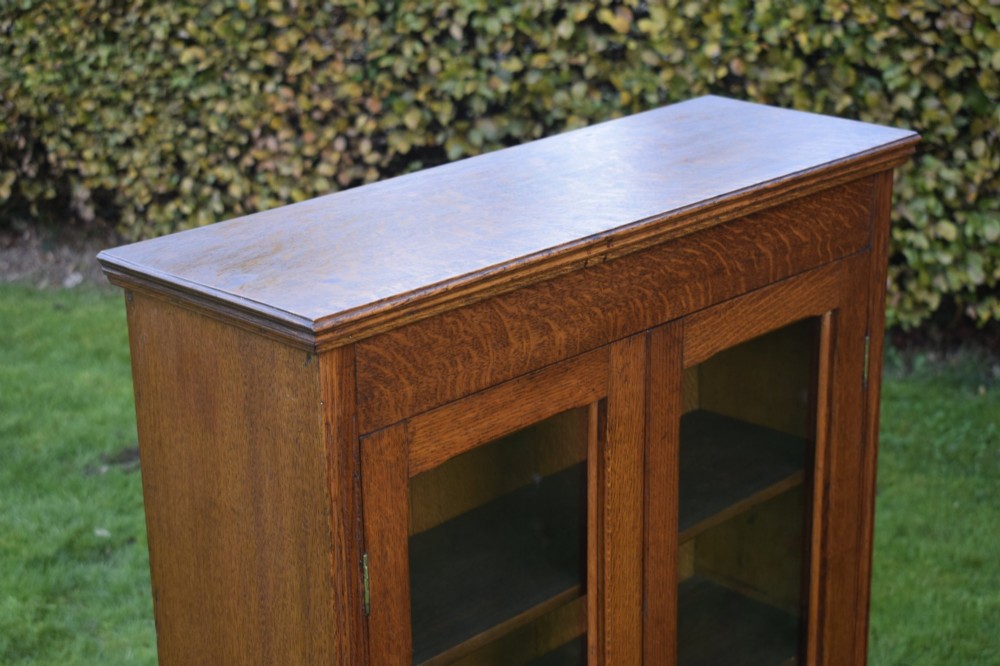 An early twentieth-century warm brown oak bookcase featuring twin glazed doors, brass hardware, and three internal shelves. View XI