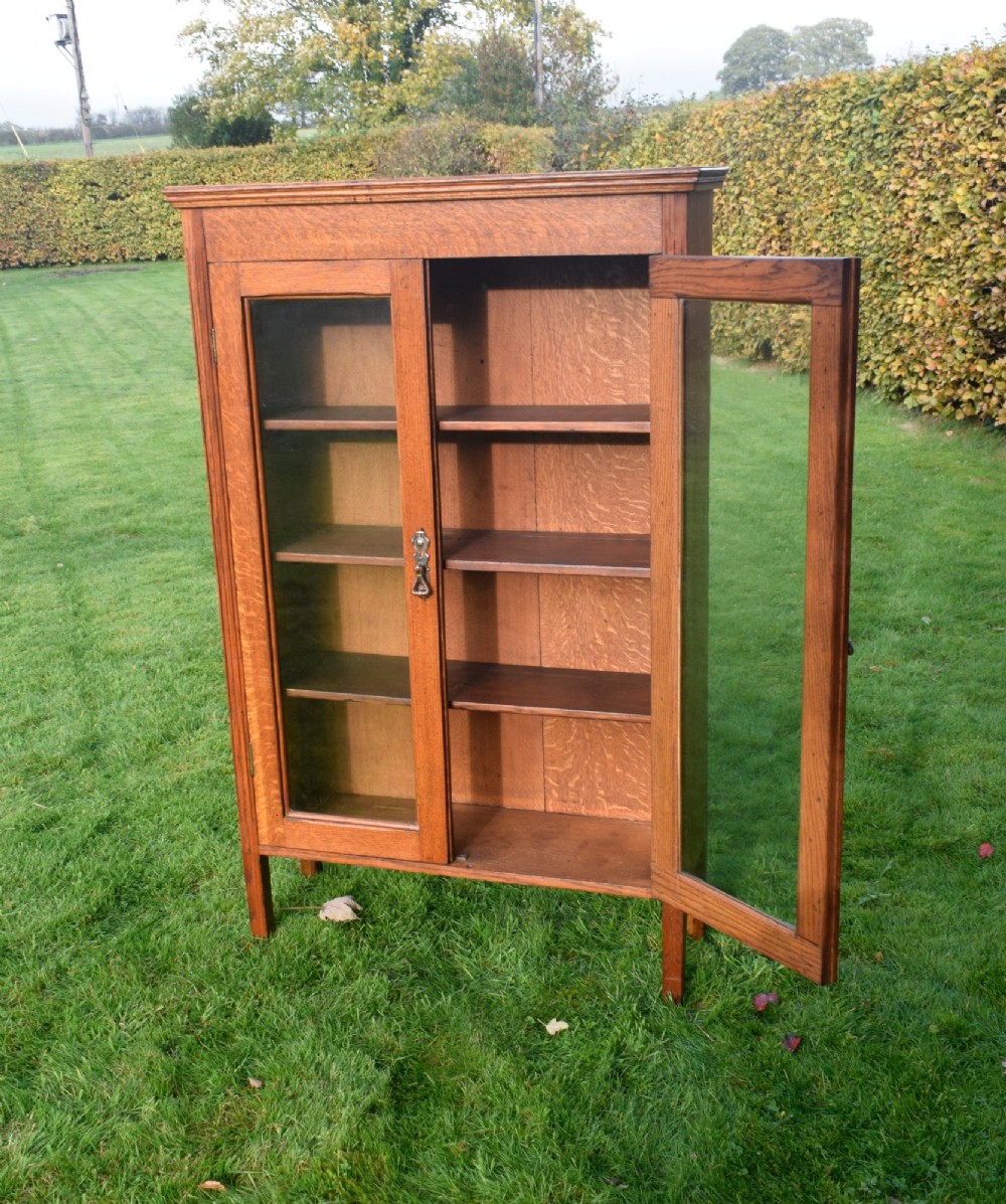 An early twentieth-century warm brown oak bookcase featuring twin glazed doors, brass hardware, and three internal shelves. View XIV