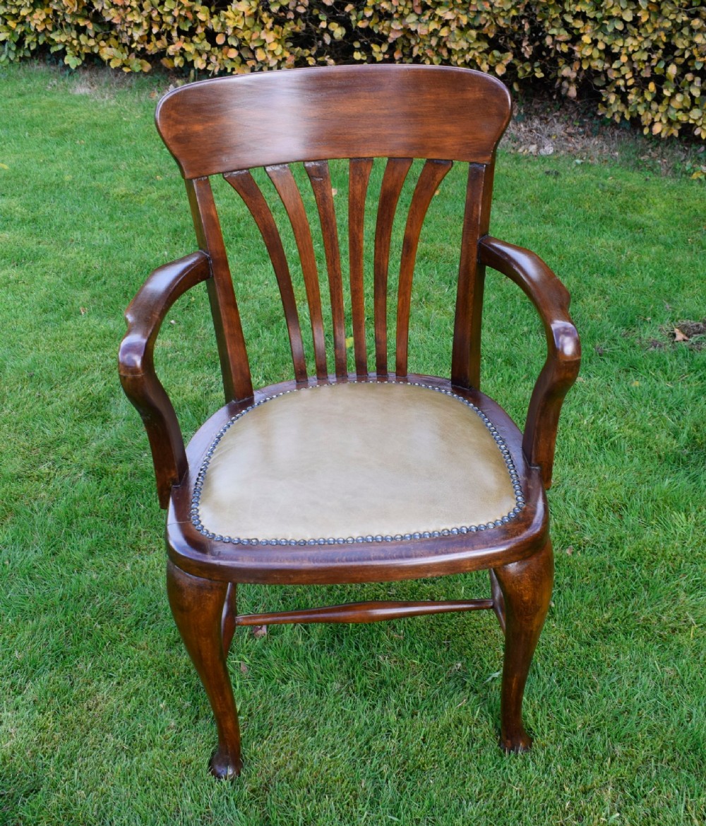 A late Victorian wooden desk armchair with a curved slatted backrest, curved arms, and a tan leather seat trimmed with studding. View II