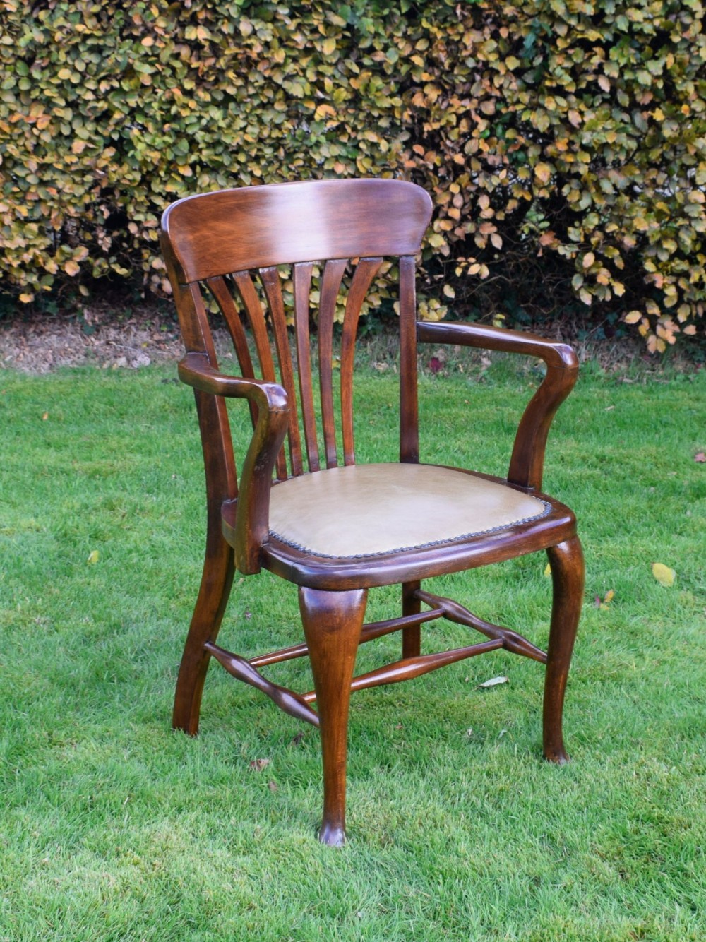A late Victorian wooden desk armchair with a curved slatted backrest, curved arms, and a tan leather seat trimmed with studding. View III
