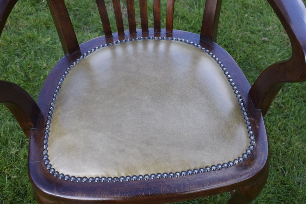 A late Victorian wooden desk armchair with a curved slatted backrest, curved arms, and a tan leather seat trimmed with studding. View IV