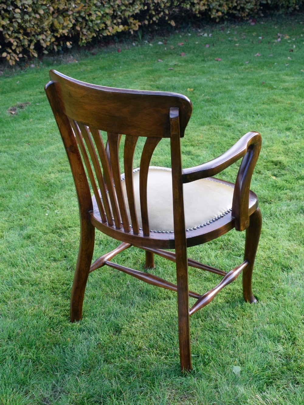 A late Victorian wooden desk armchair with a curved slatted backrest, curved arms, and a tan leather seat trimmed with studding. View V