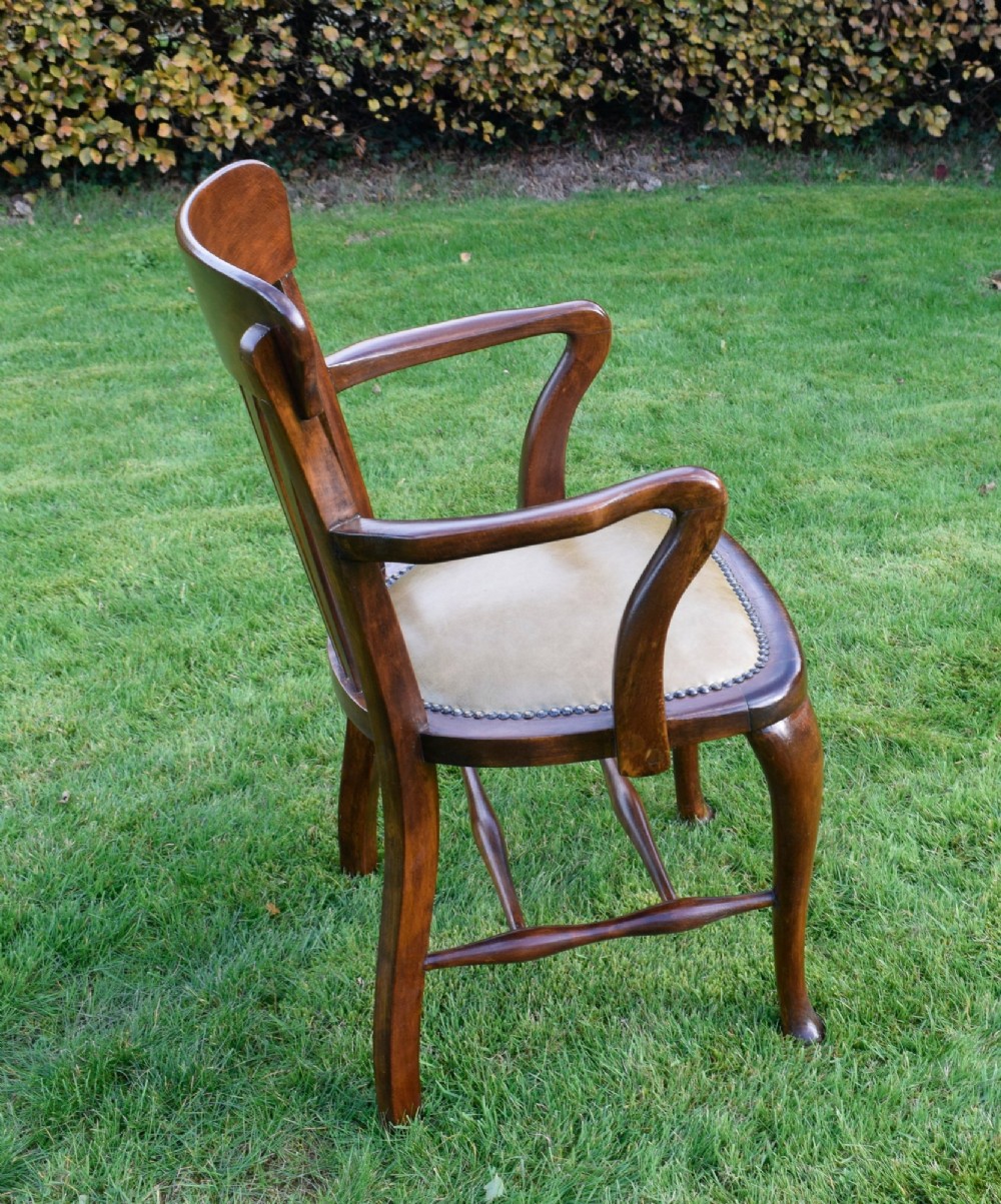 A late Victorian wooden desk armchair with a curved slatted backrest, curved arms, and a tan leather seat trimmed with studding. View VI