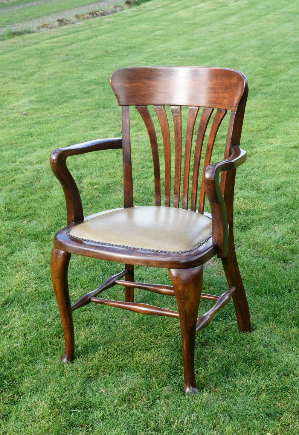 A late Victorian wooden desk armchair with a curved slatted backrest, curved arms, and a tan leather seat trimmed with studding. View VII