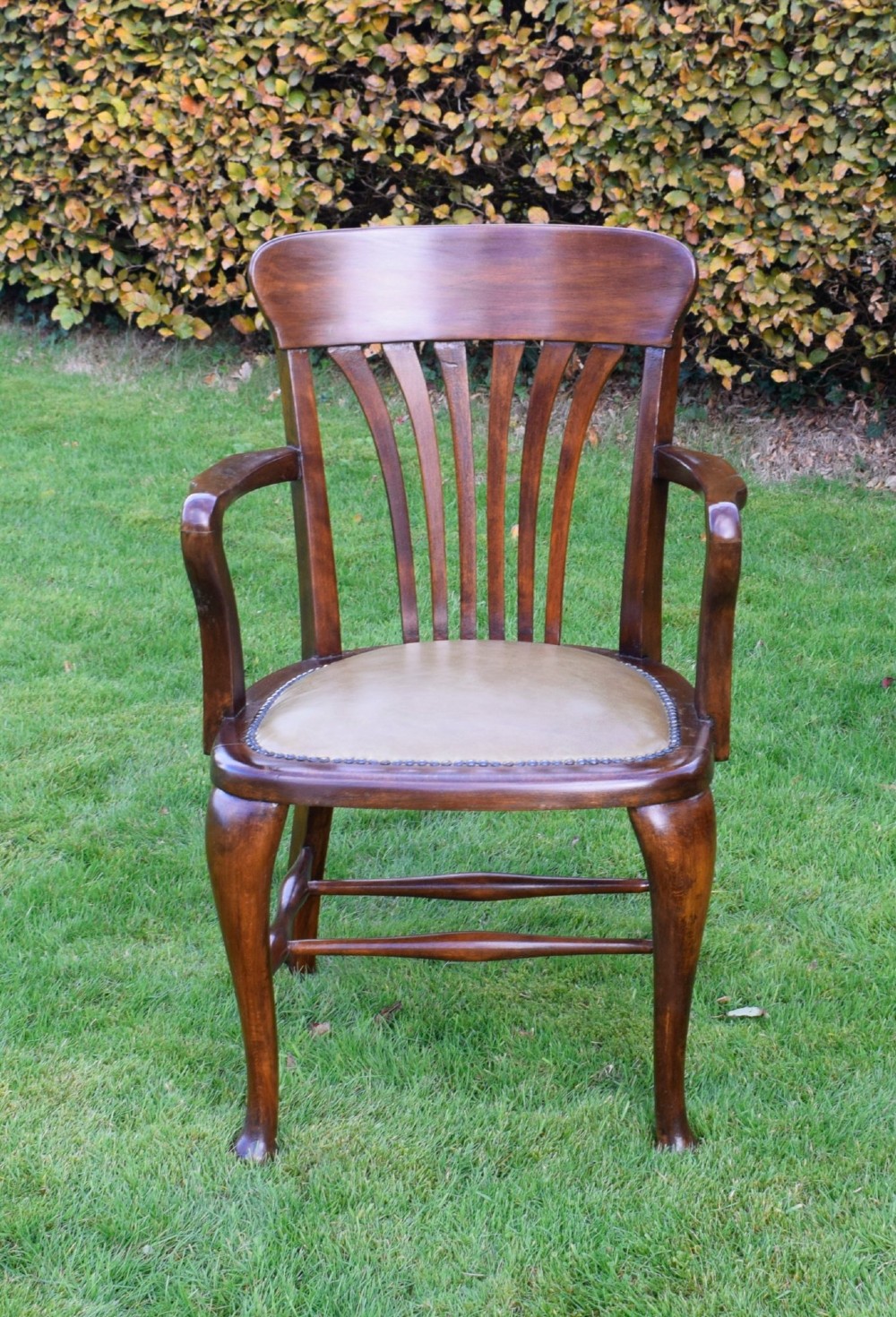 A late Victorian wooden desk armchair with a curved slatted backrest, curved arms, and a tan leather seat trimmed with studding. View XII