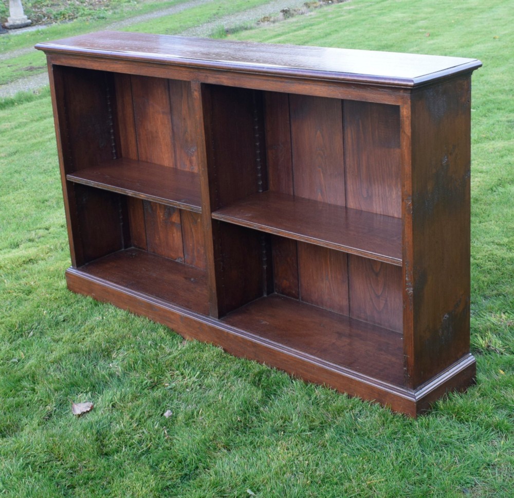 A wide early 20th-century low open oak bookcase with two main compartments, a central vertical divider, plank backboard, and a moulded top edge. View IV