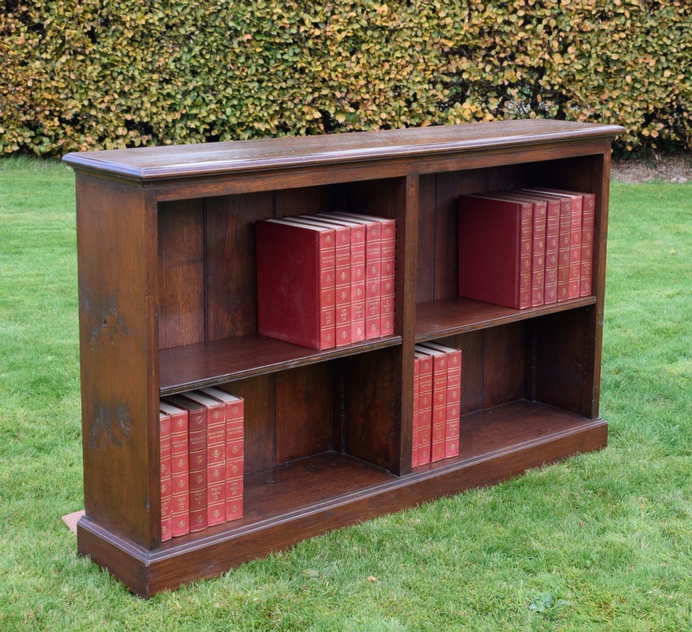A wide early 20th-century low open oak bookcase with two main compartments, a central vertical divider, plank backboard, and a moulded top edge. View V