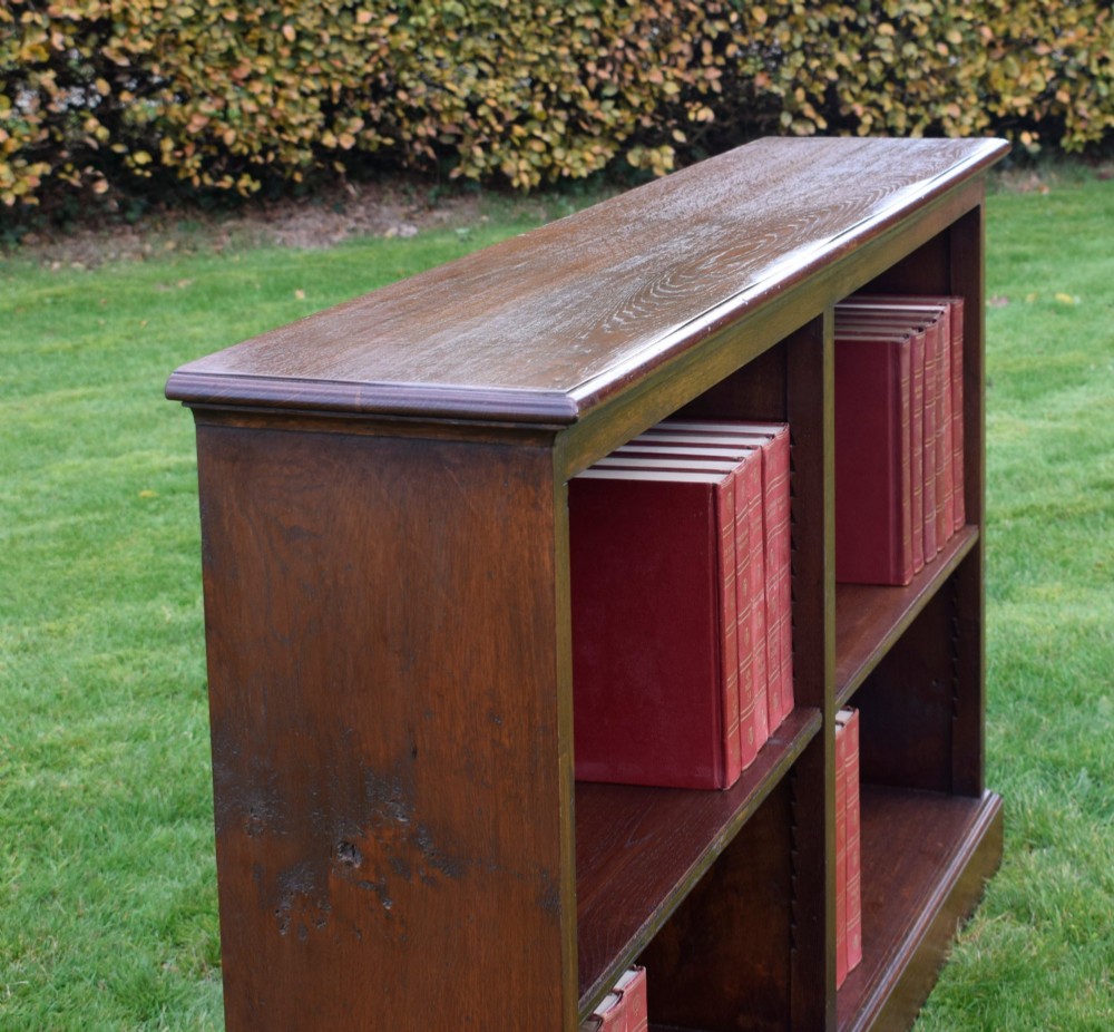 A wide early 20th-century low open oak bookcase with two main compartments, a central vertical divider, plank backboard, and a moulded top edge. View VI
