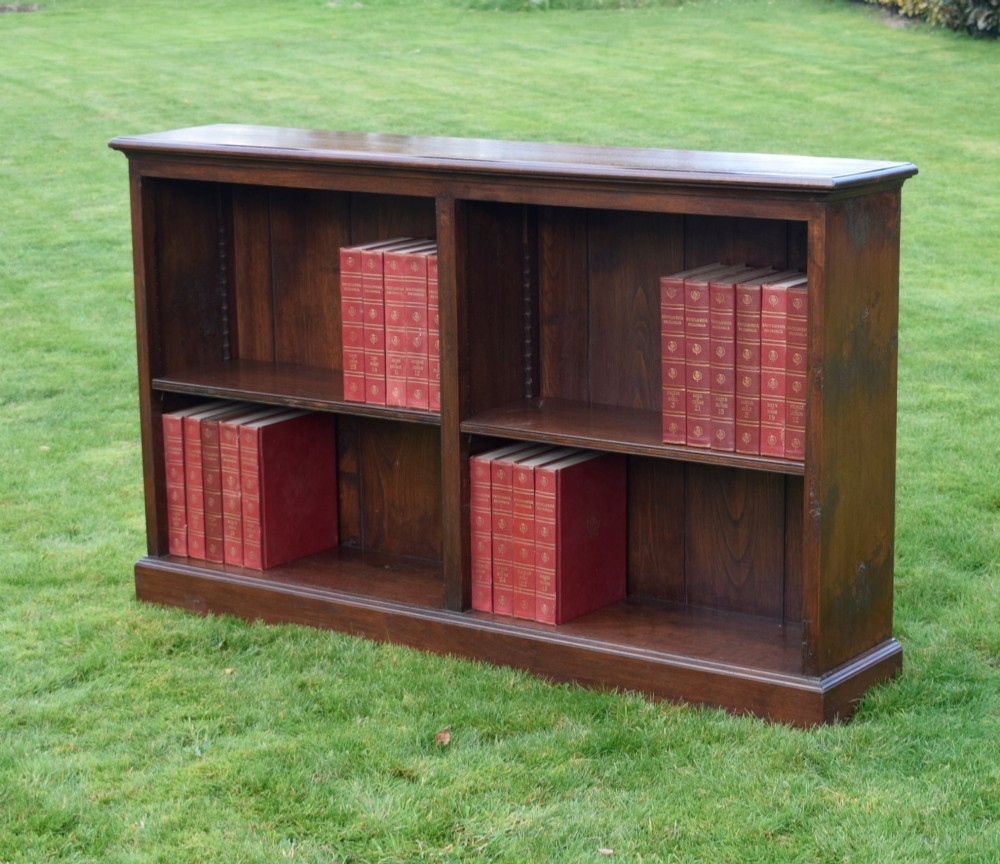 A wide early 20th-century low open oak bookcase with two main compartments, a central vertical divider, plank backboard, and a moulded top edge. View VIII
