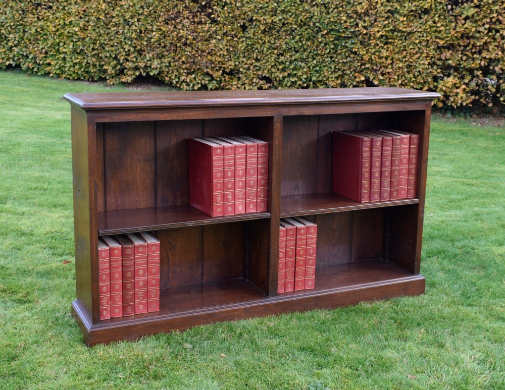A wide early 20th-century low open oak bookcase with two main compartments, a central vertical divider, plank backboard, and a moulded top edge. View X