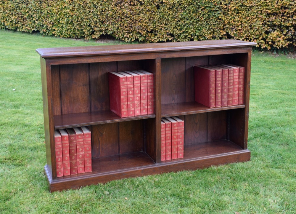 A wide early 20th-century low open oak bookcase with two main compartments, a central vertical divider, plank backboard, and a moulded top edge. View XI