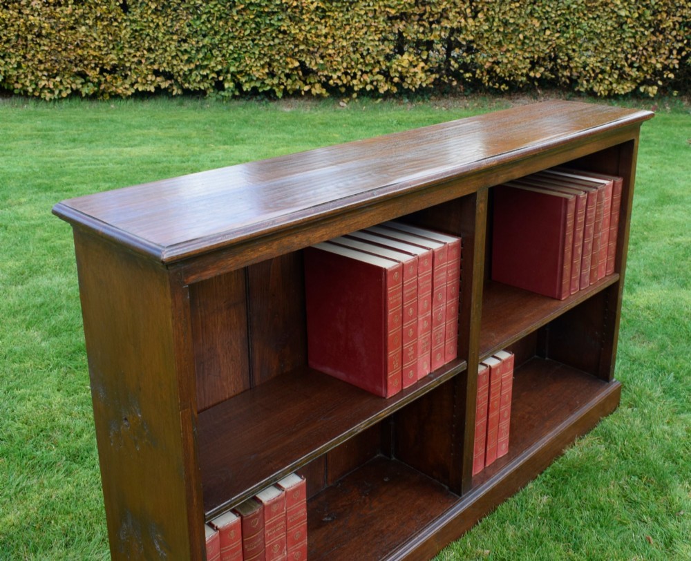 A wide early 20th-century low open oak bookcase with two main compartments, a central vertical divider, plank backboard, and a moulded top edge. View XIII