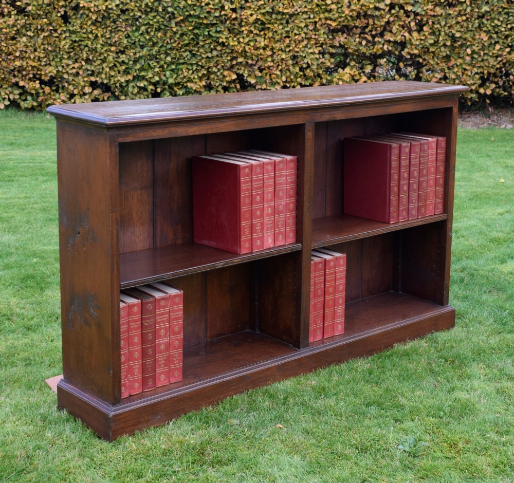 A wide early 20th-century low open oak bookcase with two main compartments, a central vertical divider, plank backboard, and a moulded top edge. View XV