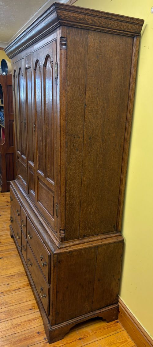 An antique George III oak housekeepers cupboard with arched fielded panels on the top doors above a base of drawers with brass handles. View VII